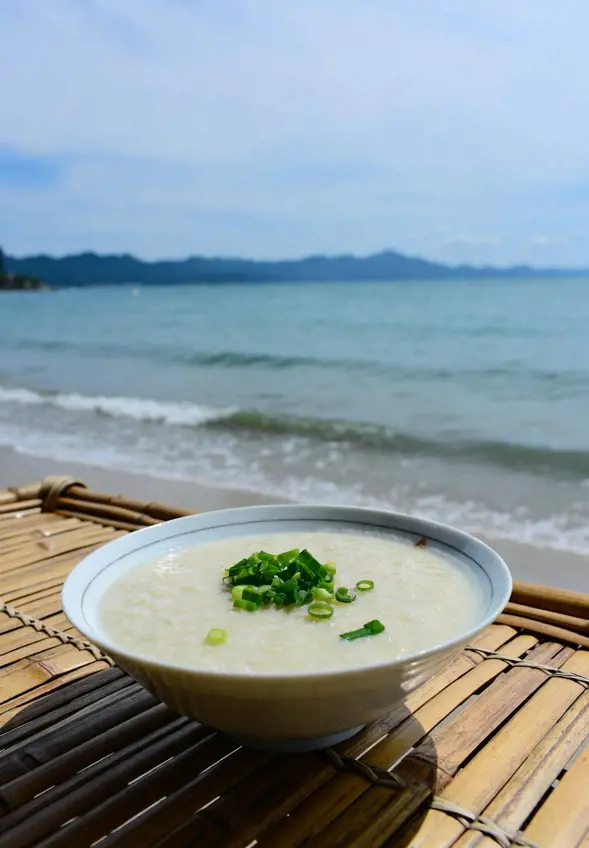 A bowl of conjee (rice porridge) on a bamboo table by the sea