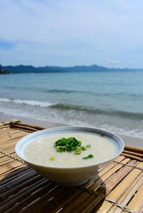 A bowl of conjee (rice porridge) on a bamboo table by the sea